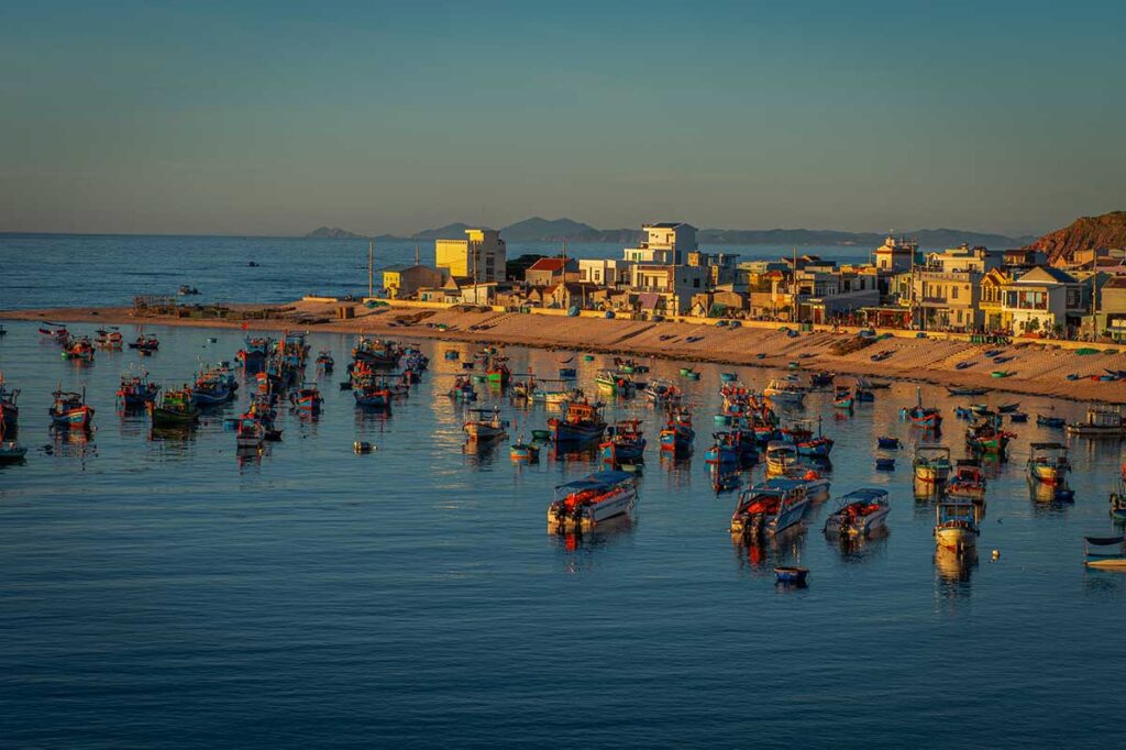Nhon Hai fishing boats at dusk – Dozens of colorful wooden boats anchored offshore as golden evening light falls on the village.