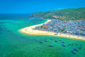 Aerial view of Nhon Hai Fishing Village – Bright turquoise water, sandy coastline, and fishing boats surrounding the densely packed houses on the peninsula.