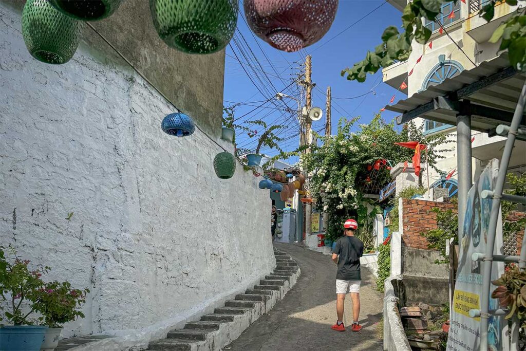 Steep blue-and-white lane in Nhon Ly village on Phuong Mai Peninsula, lanterns and stone steps above the sea.