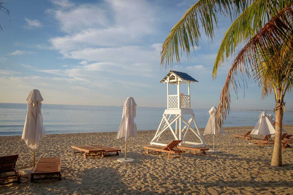 Empty sun loungers and lifeguard tower on Ninh Chu Beach, Phan Rang, during a calm morning.