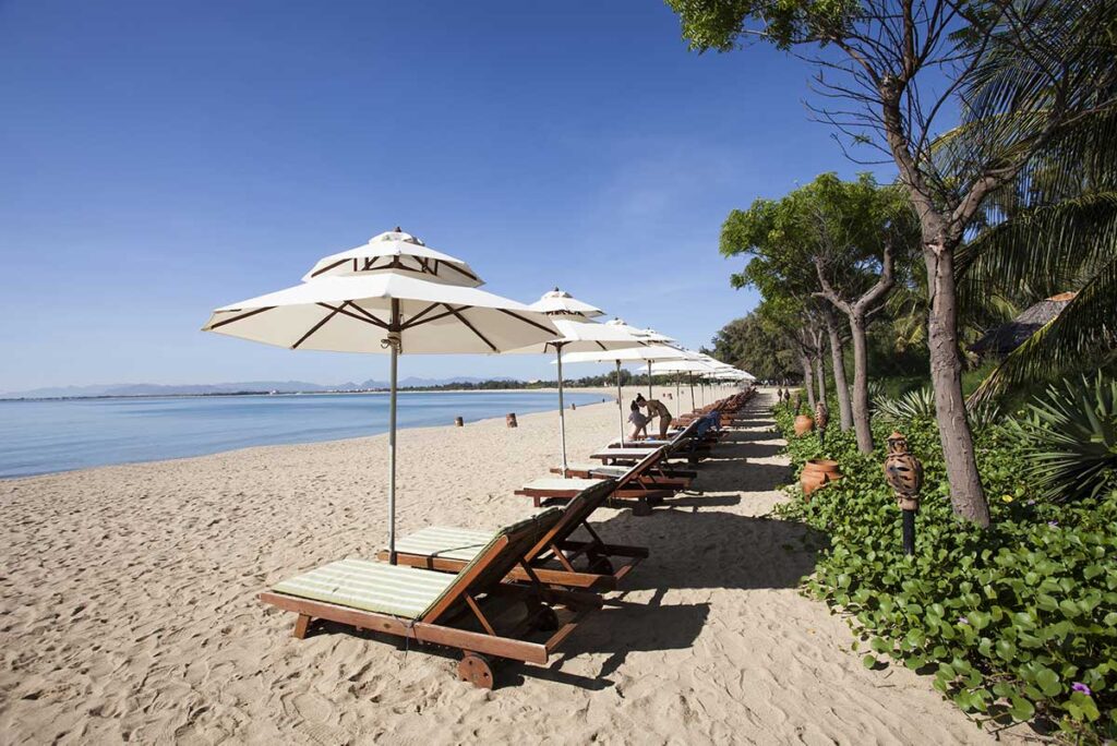Row of sun loungers and parasols along the sandy shoreline of Ninh Chu Beach, Phan Rang, on a clear sunny day