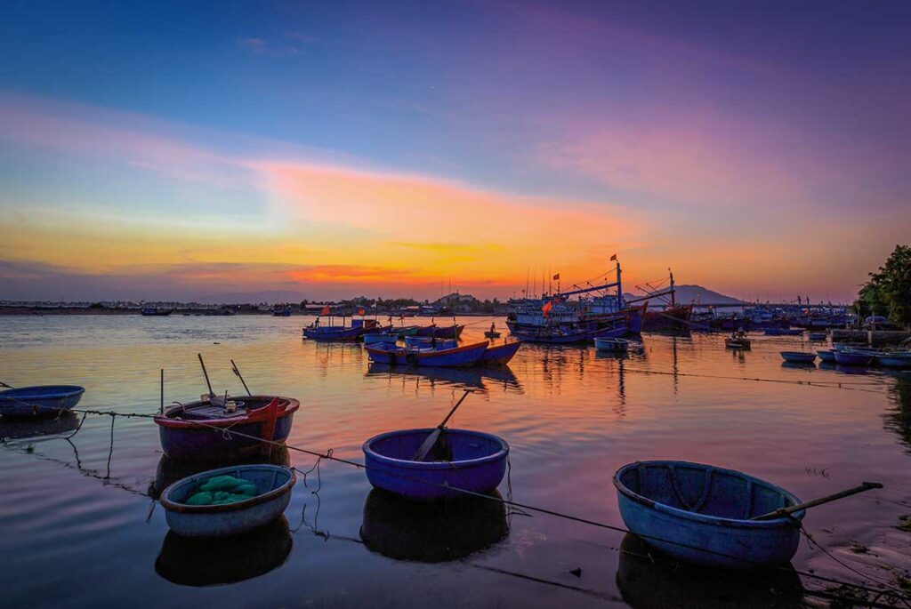 Fishing boats and round basket boats anchored at Ninh Chu fishing port at sunset, Phan Rang, Ninh Thuan.
