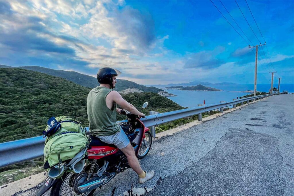 Traveler on motorbike along the coastal road DT702 in Nui Chua National Park, overlooking the sea and rugged mountains of Ninh Thuan.