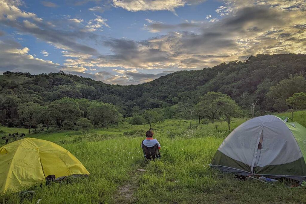 Backpacker camping in Nui Chua National Park, surrounded by green hills and forest valleys under a dramatic evening sky.
