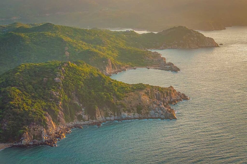 Aerial view of Nui Chua National Park’s rocky headlands and turquoise bays at sunset, highlighting the untouched coastline of Ninh Thuan.