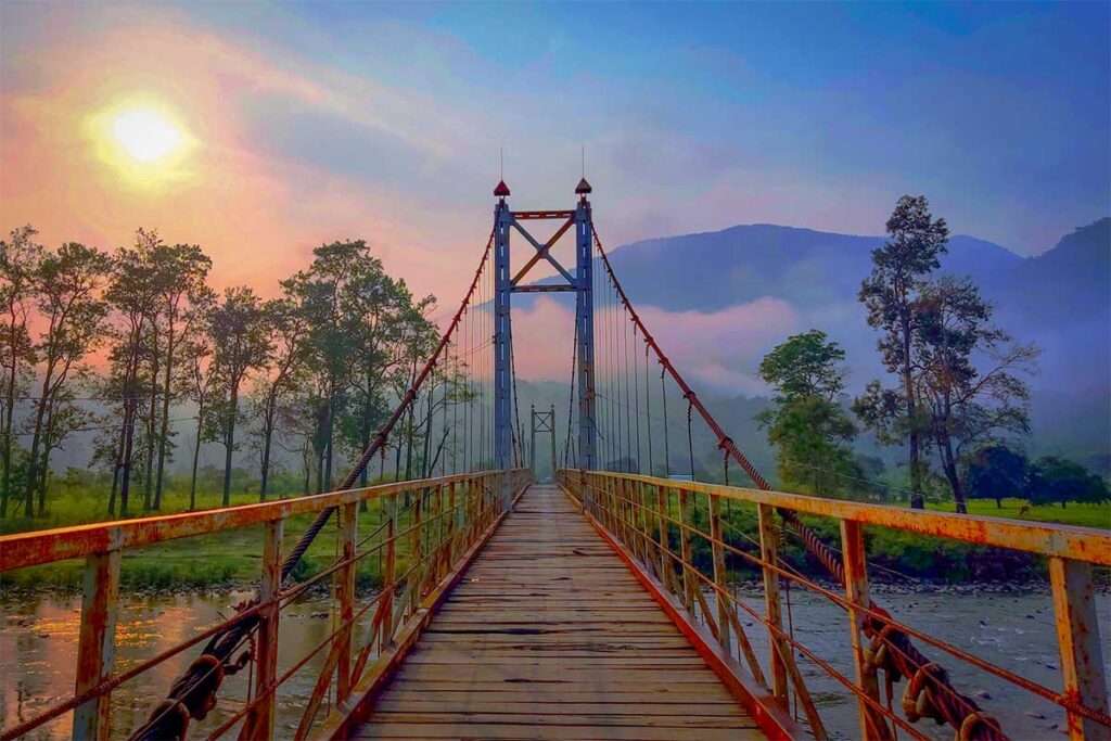 Suspension bridge in Phuoc Binh National Park – Rustic wooden bridge crossing a river at sunrise with misty mountains in the background.