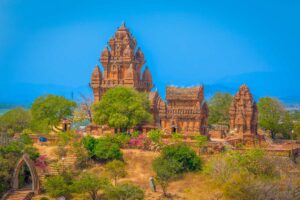 Panoramic view of Po Klong Garai Tower complex in Phan Rang, Vietnam, with red-brick Cham temples standing on Trau Hill surrounded by dry landscape and clear blue skies.