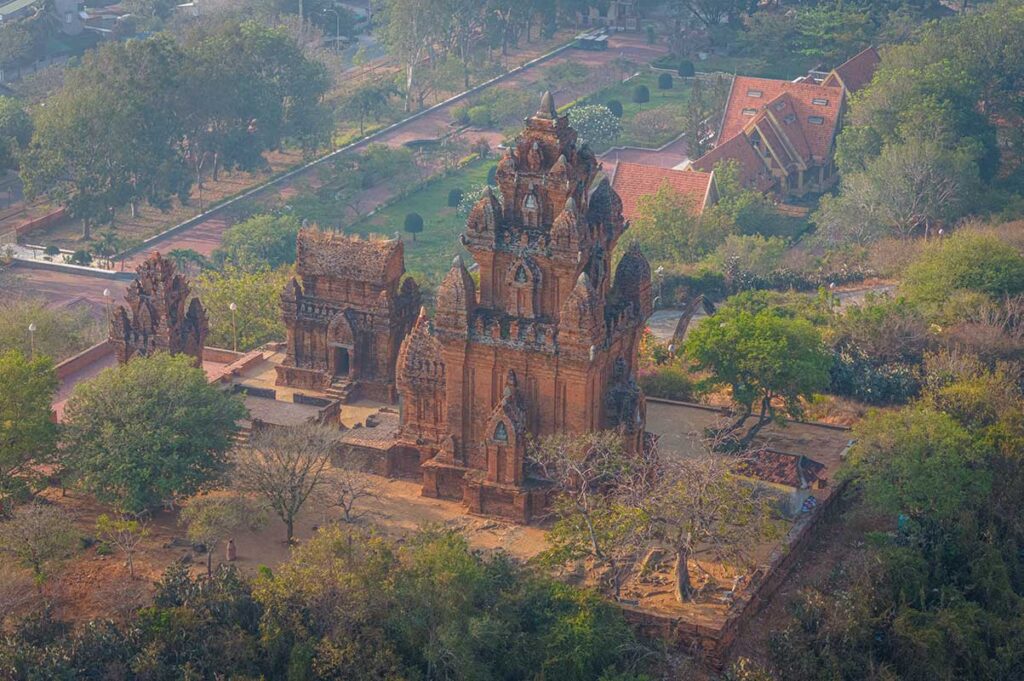 Aerial view of the Po Klong Garai Cham Tower complex in Phan Rang, with three main red-brick towers surrounded by trees and city landscape.