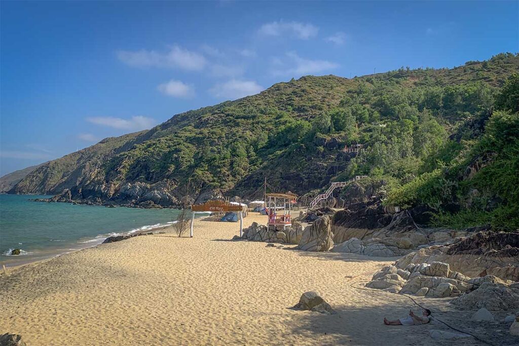 Sandy shore at Rang Beach, Quy Nhon with rustic stairs, rocky cliffs and a secluded coastline feel.