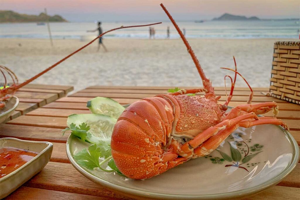 Seafood dinner at Vinh Hoa Beach — fresh local lobster served beachfront at sunset.