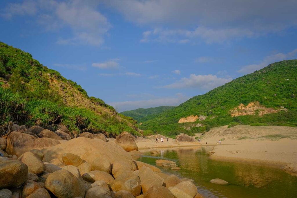 Freshwater stream running across Bai Mon Beach in Phu Yen, Vietnam, with sandy dunes and green hills in the background.