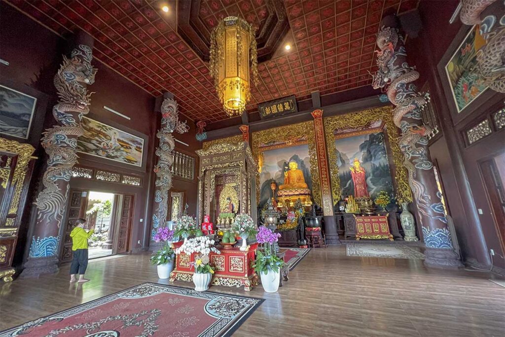 Interior of the main worship hall at Thien Hung Pagoda with Buddha statues, dragon pillars, and golden decorations.