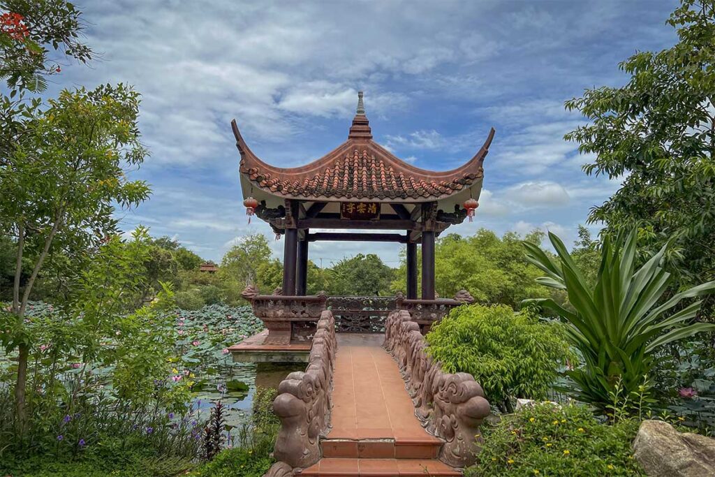 Lotus pond pavilion at Thien Hung Pagoda in Binh Dinh, reached by an ornate stone bridge surrounded by greenery.