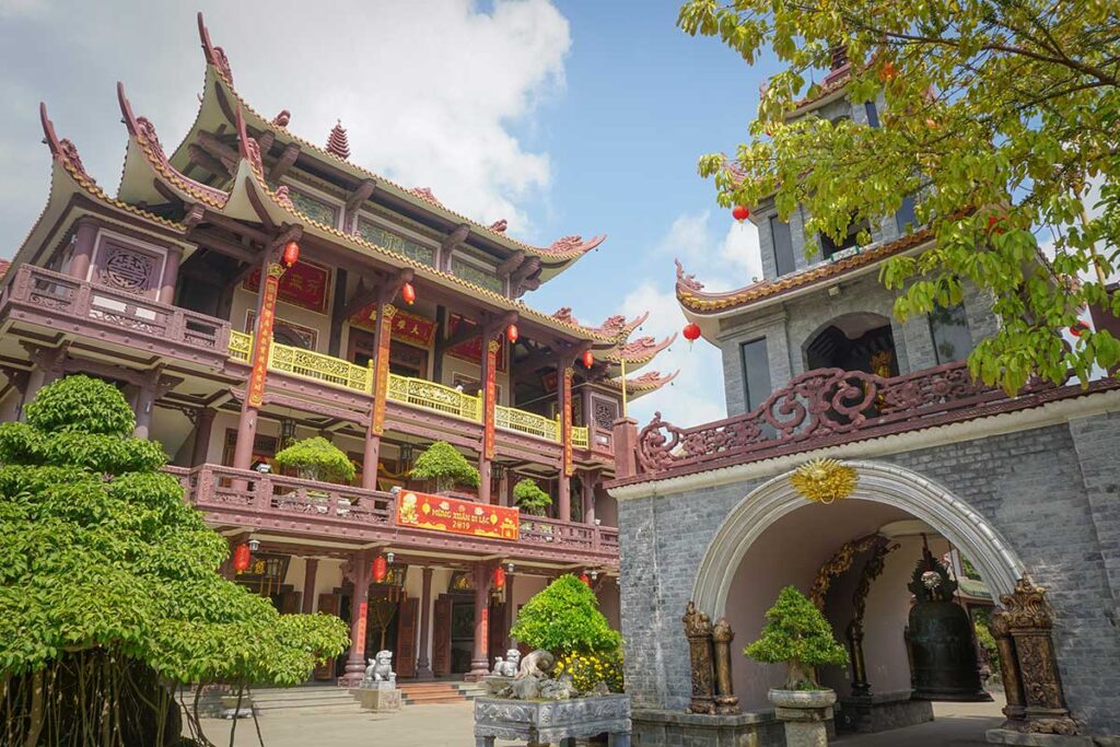 Front view of Thien Hung Pagoda main building and bell tower decorated with lanterns and bonsai trees.