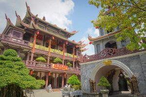 Front view of Thien Hung Pagoda main building and bell tower decorated with lanterns and bonsai trees.