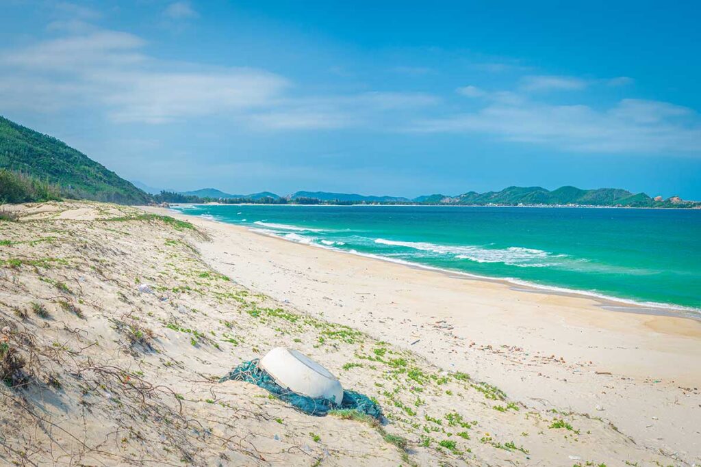 Remote dunes and empty sands at Tu Nham Beach, Phu Yen, with turquoise water and mountain backdrop.