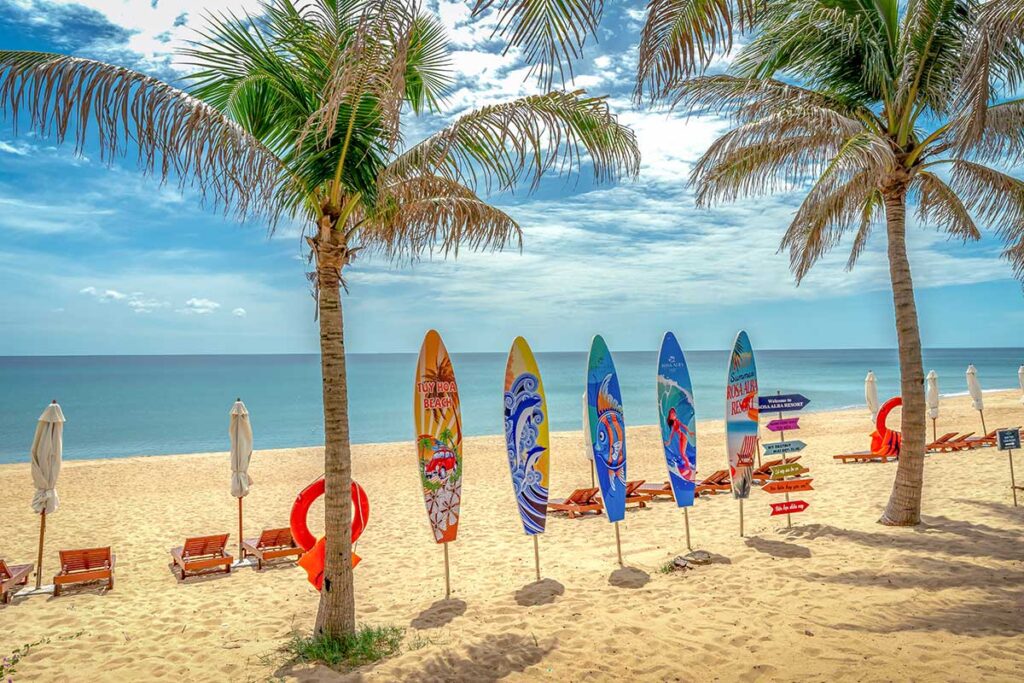 Palm-lined section of Tuy Hoa City Beach with surfboards as decoration and loungers set up along the sand.