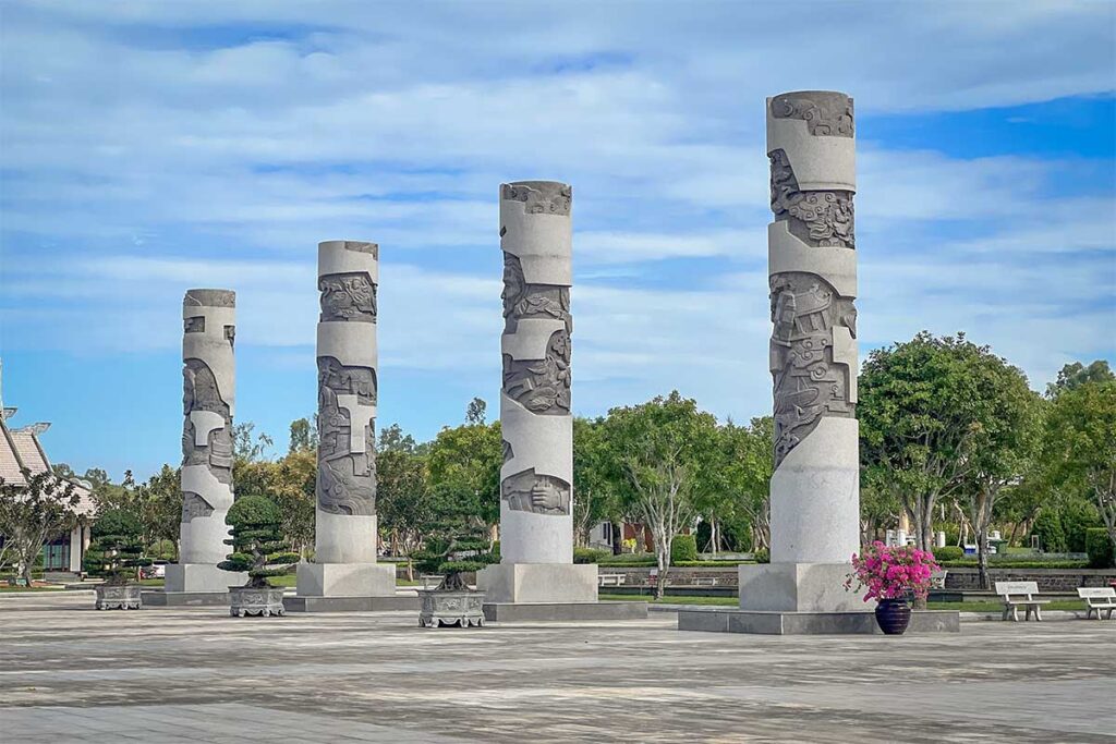 Stone pillars with carvings at the Vietnamese Heroic Mother Statue in Tam Ky, representing mothers and young volunteers from different regions of Vietnam.