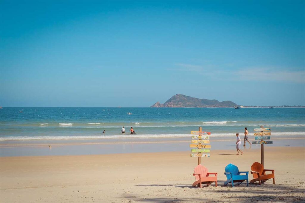 Family-friendly shoreline at Vinh Hoa Beach with calm waves, island backdrop, and beach chairs.