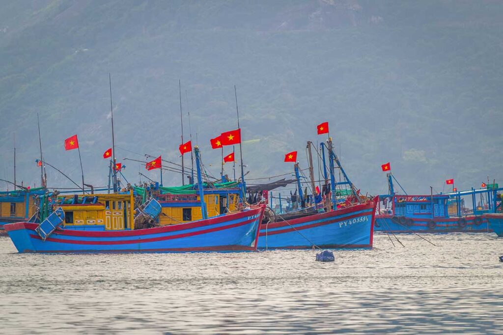 Fishing boats flying Vietnam flags anchored off Vinh Hoa Fishing Village, a coastal community on Tu Nham Bay.