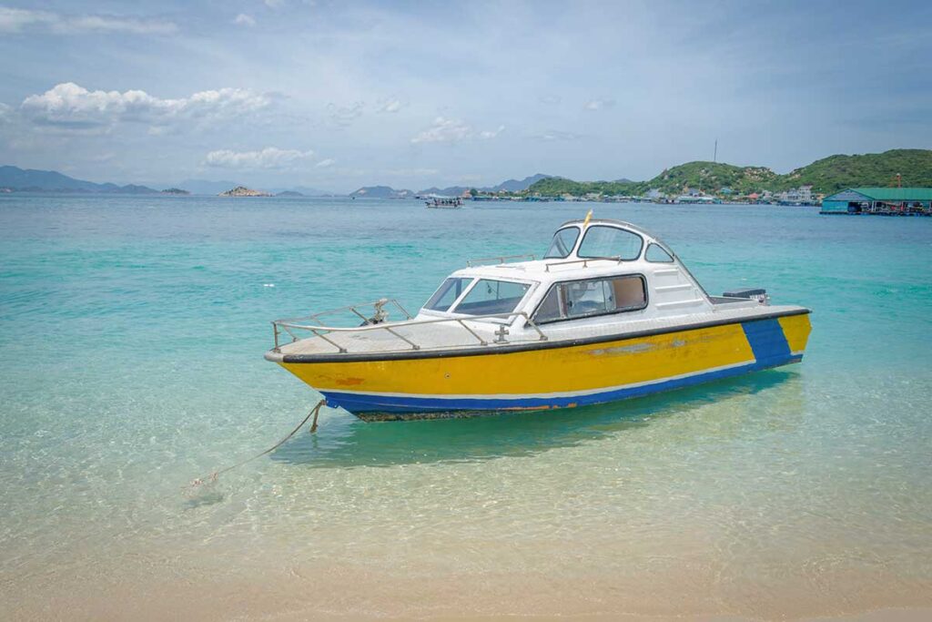 Yellow boat on the clear blue water of Vinh Hy Bay – A small motorboat anchored on a pocket beach with crystal-clear water and green hills in the background, typical of Vinh Hy Bay’s fishing coast.