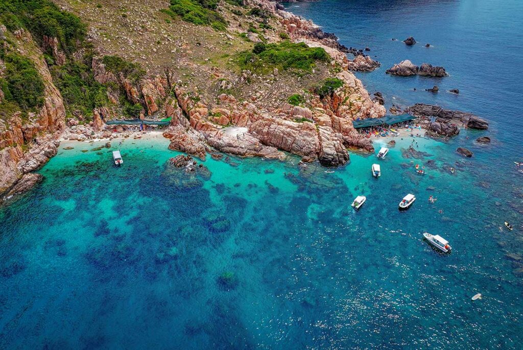 Tour boat cruising through Vinh Hy Bay’s blue waters – Local wooden boat carrying passengers past rocky headlands and hidden coves, a typical way to explore the bay.