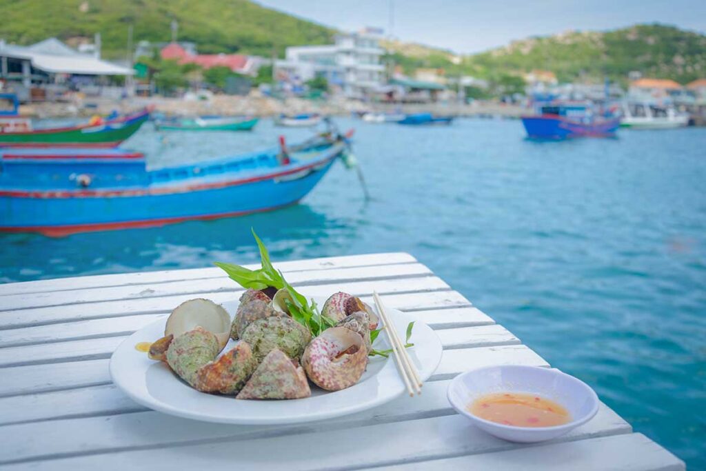 Seafood lunch on floating restaurant in Vinh Hy Bay – Fresh shellfish served with dipping sauce on a simple table overlooking the fishing harbor, a typical dining experience in Vinh Hy Bay.