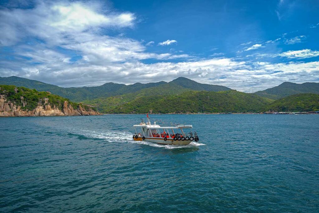 Glass-bottom tour boat in Vinh Hy Bay waters – A sightseeing boat cruising through the bay with rocky cliffs and Nui Chua mountains in the background, used for snorkeling and coastal trips.