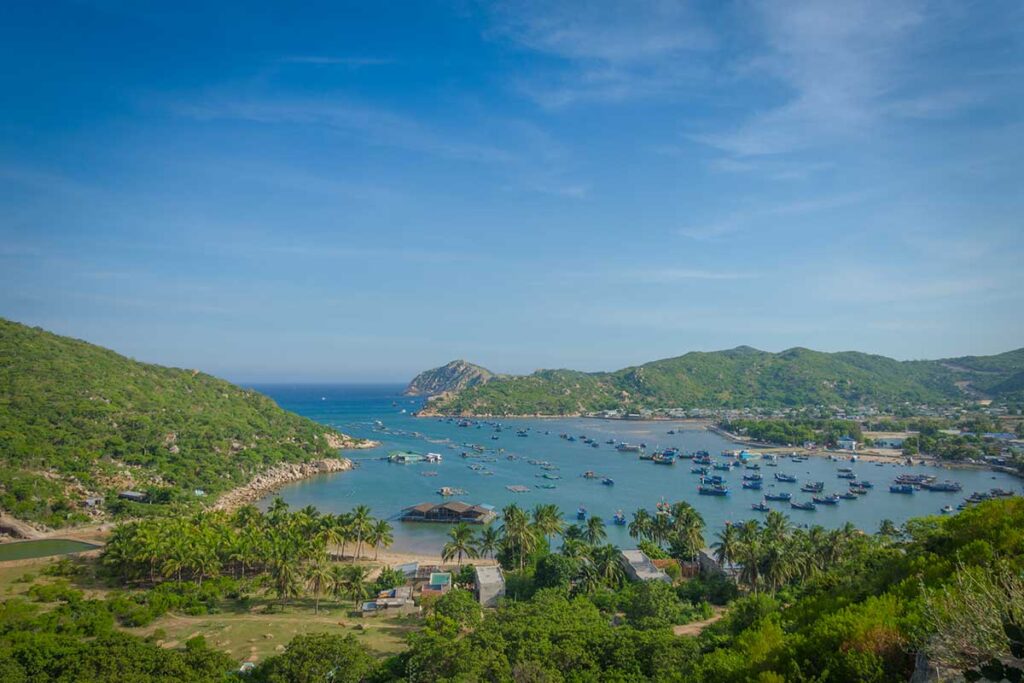 Panoramic view of Vinh Hy Bay in Nui Chua National Park, dotted with fishing boats and surrounded by lush green hills.