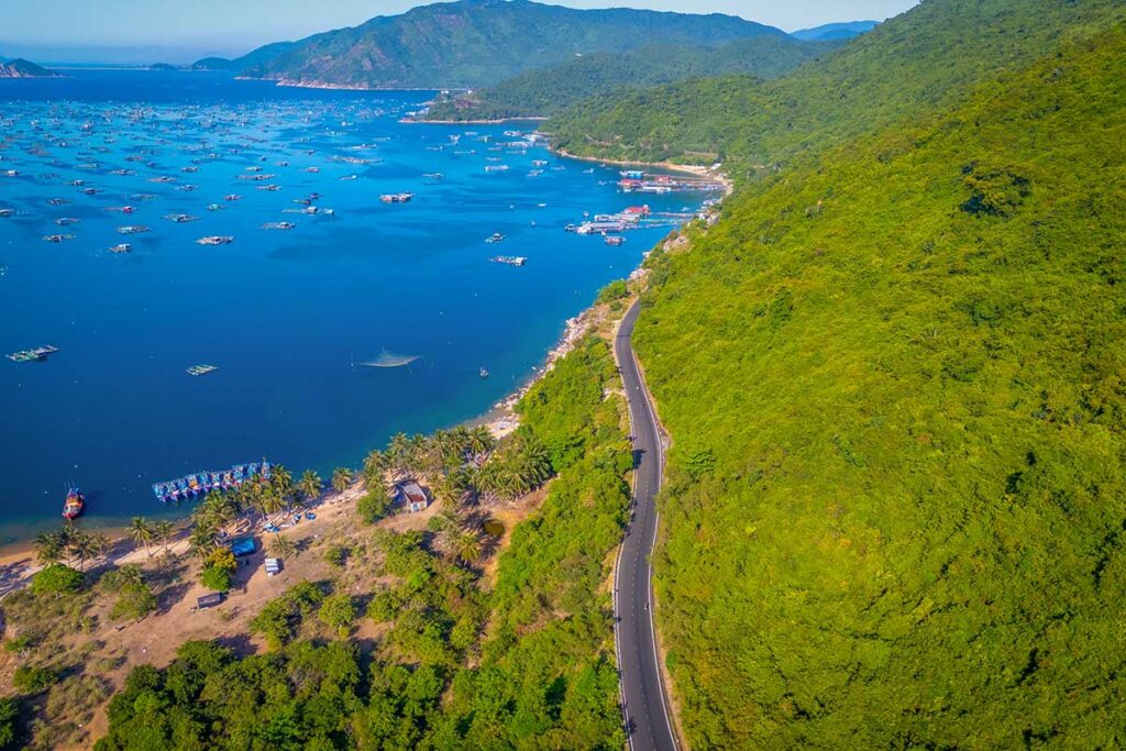 Scenic coastal road winding along Vung Ro Bay, framed by palm trees, fishing boats, and turquoise water.