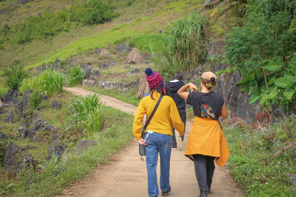 Travelers walking on a small mountain path during a local trekking experience in Ha Giang.