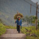 Elderly ethnic woman carrying a basket on a mountain trail near Ha Giang Aya Lodge.