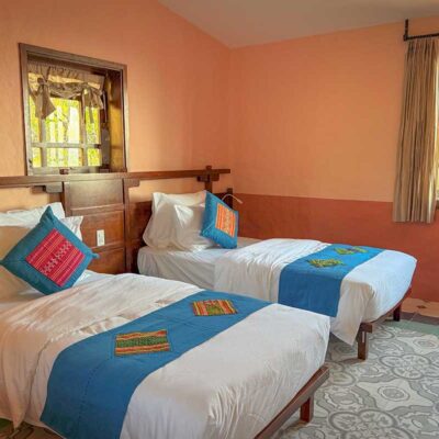 Twin-bed setup in the Deluxe Room at Ha Giang Aya Lodge with warm decor and hillside views.