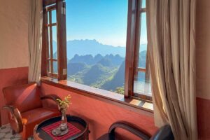 Sitting corner in the Deluxe Room at Ha Giang Aya Lodge with open window and panoramic mountain views.