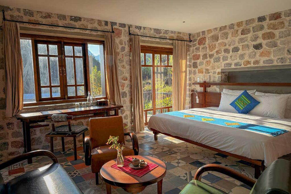 Stone-wall room at Ha Giang Aya Lodge with sunlight, wooden furniture and valley views.