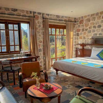 Stone-wall room at Ha Giang Aya Lodge with sunlight, wooden furniture and valley views.