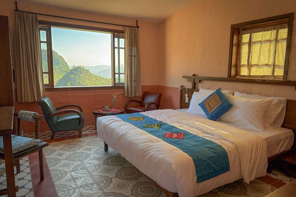 Cozy room at Ha Giang Aya Lodge with mountain view through large open window.