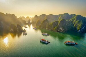 Boats sailing among limestone islands in Halong Bay at sunrise — a breathtaking highlight featured in many Vietnam tours and Vietnam itineraries.