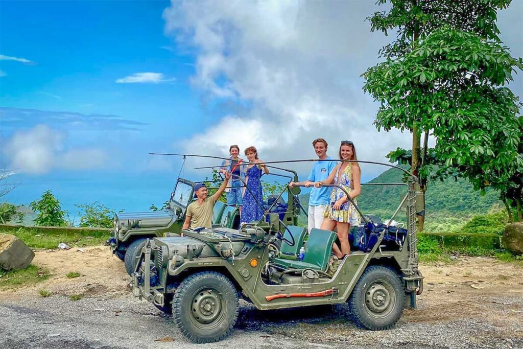 Travelers enjoying a vintage jeep ride on Hai Van Pass — a unique alternative to standard Vietnam car rental with driver for adventurous sightseeing.