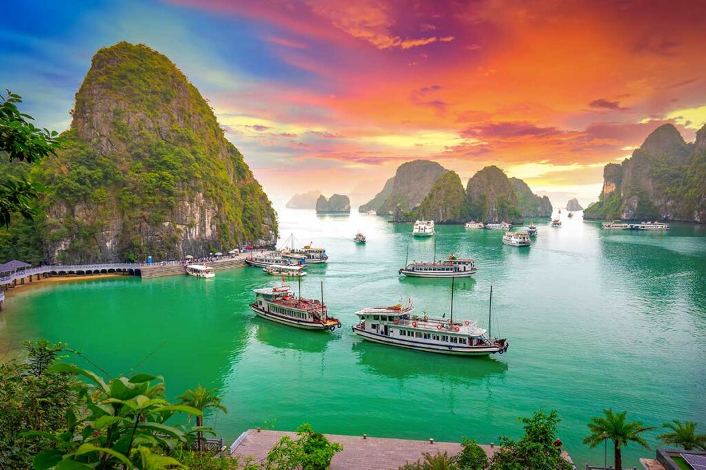Cruise boats sailing through limestone islands at sunset in Halong Bay, a must-see destination on every North Vietnam tour.
