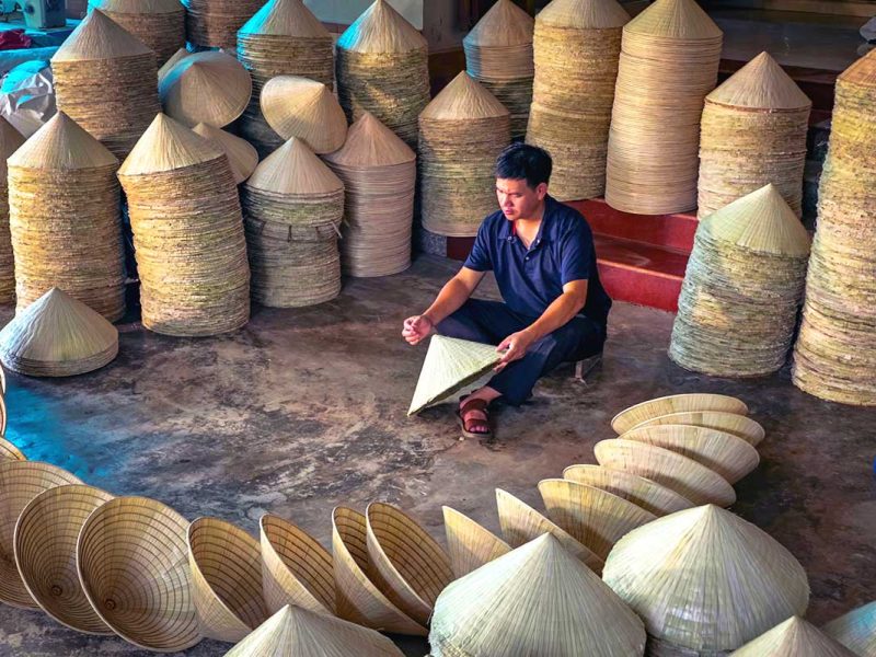 a man holding a conical hats at a warehouse full of conical hats at Chuong Village near Hanoi