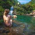 A girl sitting in a bikini on a rock, watching people swim and jump from the rocks at Du Gia Waterfall, a