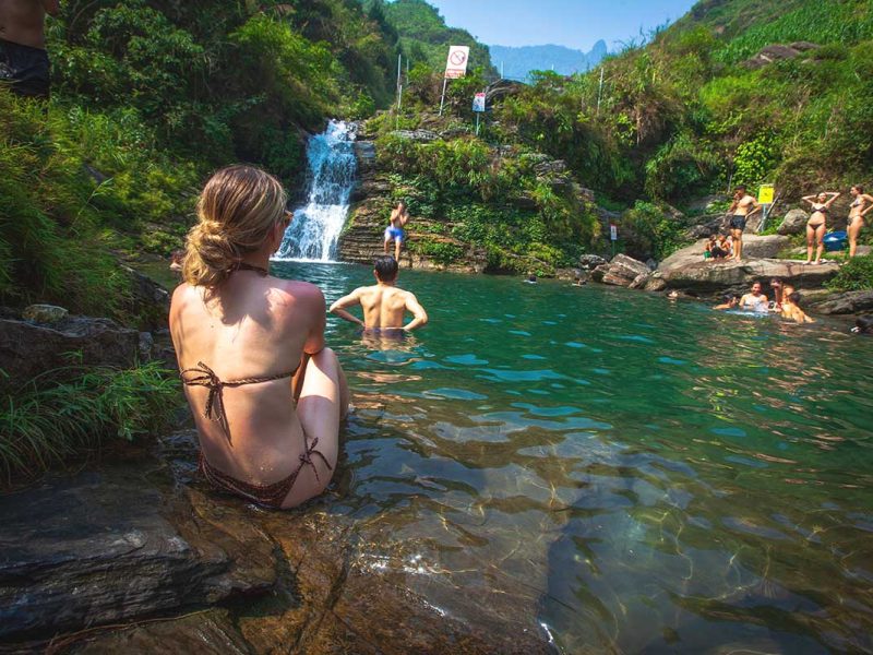 du gia waterfall girl ha giang 1 A girl sitting in a bikini on a rock, watching people swim and jump from the rocks at Du Gia Waterfall, a
