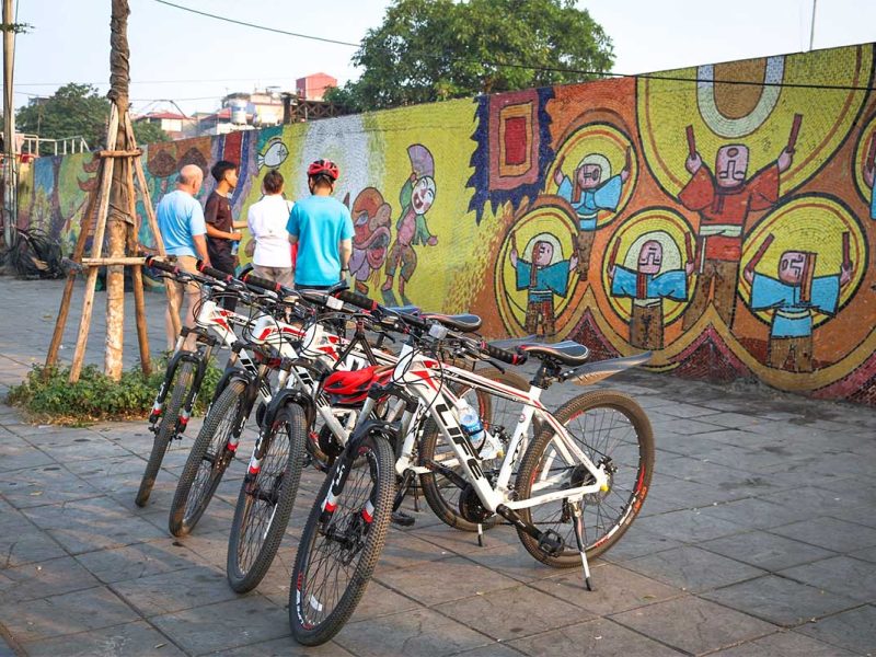 Bicycles parked near tourists and guide viewing the Hanoi mosaic wall on a cycling tour
