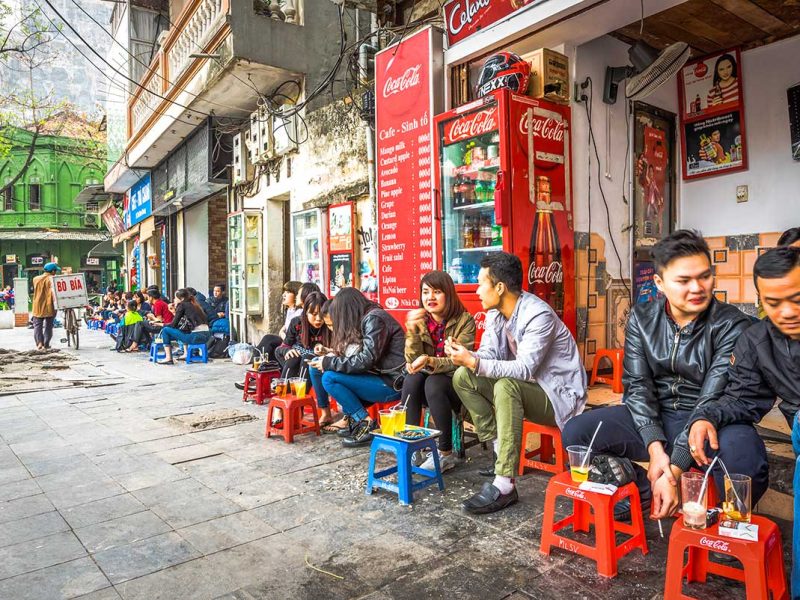 Local Street Coffee Scene in Hanoi: Locals enjoy their morning coffee on colorful plastic stools at a traditional street-side cafe in Hanoi.