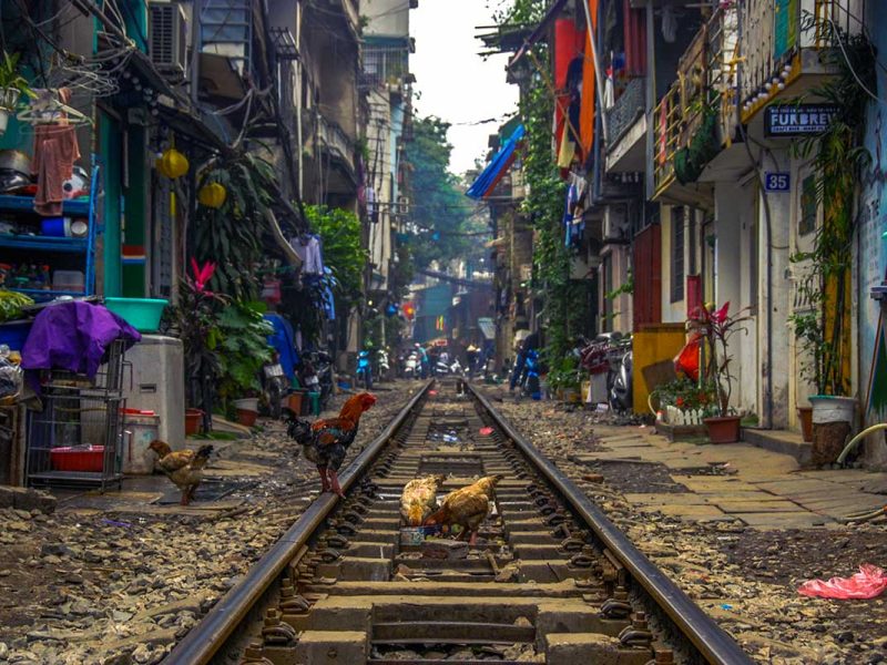 Hanoi Train Street: A train rumbles through the narrow Hanoi Train Street, passing between vibrantly colored houses.