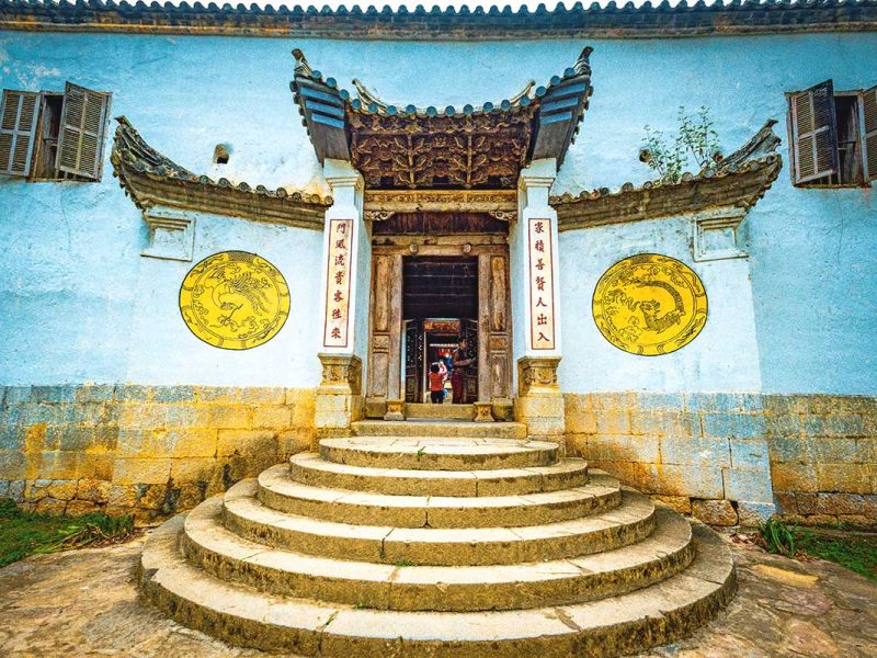 hmong king palace ha giang 3 Entrance gate of the Hmong King Palace, featuring a sturdy stone wall with white and yellow circular symbols on both sides.
