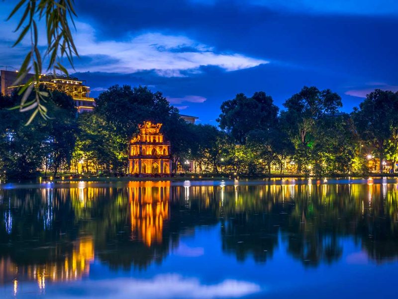 Hoan Kiem Lake at Night: The illuminated Turtle Tower shimmers on the calm waters of Hoan Kiem Lake in Hanoi, a popular nighttime photography spot. (best Instagram spots in Hanoi)
