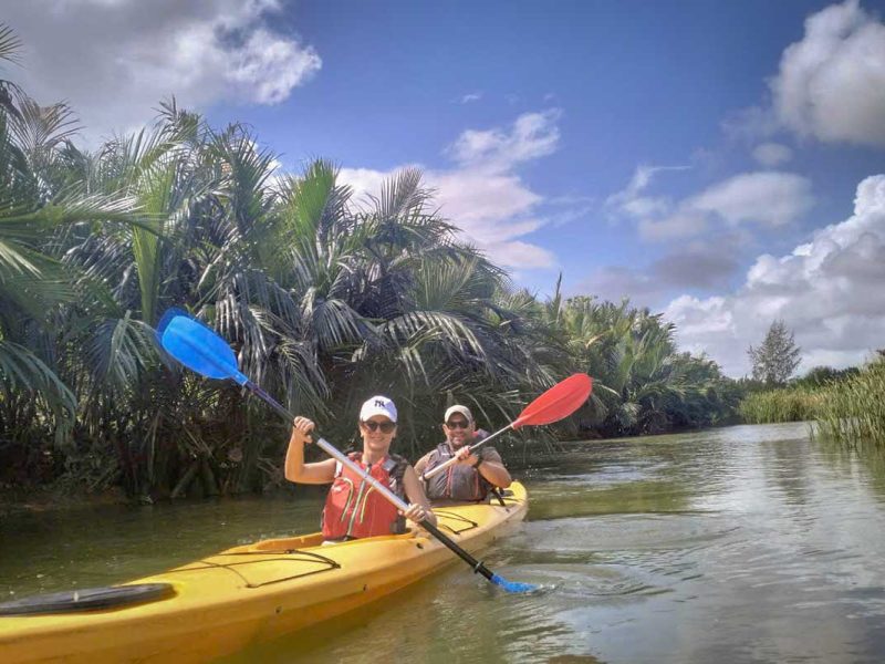 hoi an kayaking cycling tour mangrove countryside 10 Two travelers kayaking through dense nipa palm mangroves under a bright sky during the Hoi An tour