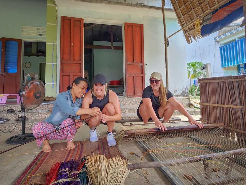 hoi an kayaking cycling tour mangrove countryside 18 Two travelers learning traditional mat weaving with a local woman during the Hoi An countryside cycling tour
